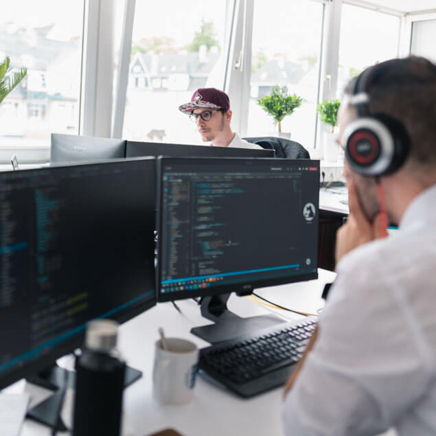 Lorent IT Mitarbeiter mit kopfhoerern vor jeweils zwei Monitoren